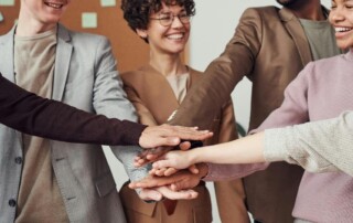 A diverse group of people holding hands in a circle in an office setting, symbolizing unity and teamwork.