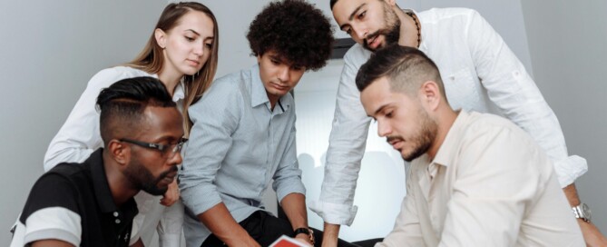 A diverse team of five colleagues gathered around a table reviewing a document together in a bright modern office